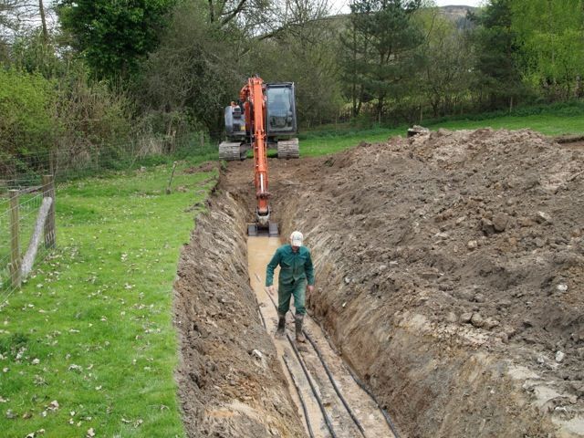 Digger and installer in a deep trench for ground source heat pump pipes