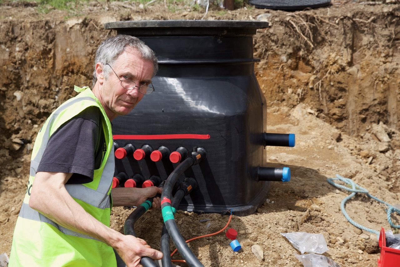 Installer connecting ground-loop pipes to a ground source manifold in a trench
