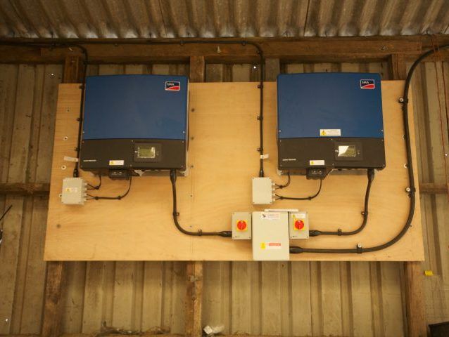 Two solar inverters and isolators mounted on a timber backboard