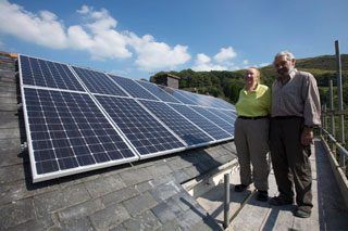 Two homeowners standing on scaffolding beside their new solar panels